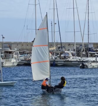 Dos jóvenes navegantes disfrutan de un día soleado en el mar, aprendiendo a controlar su velero.