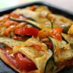 deliciosa pizza vegetariana es una opción perfecta para una comida ligera y saludable. Con una base crujiente y una combinación de verduras frescas y sabrosas, ¡esta pizza casera te conquistará! 'Pizza casera con base delgada, cubierta con salsa de tomate, rodajas de calabacín, pimiento rojo y aceitunas negras